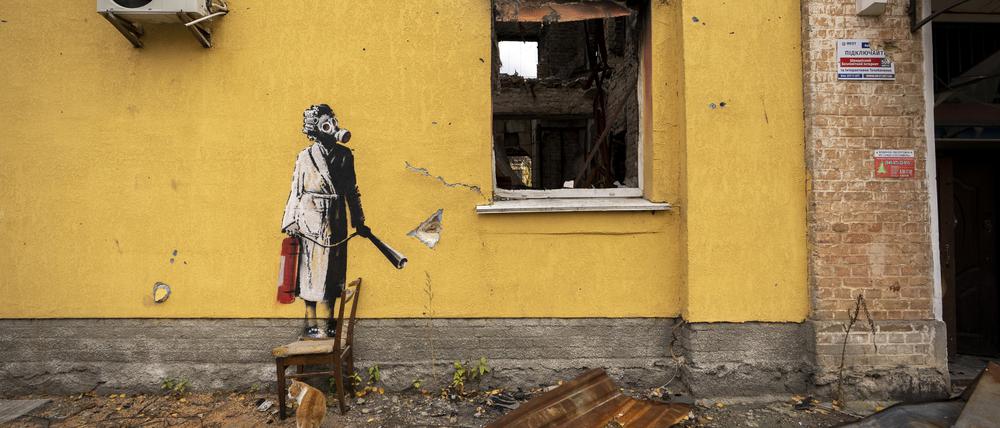 Auf der gelben Wand des Gebäudes ist ein Bild einer Person zu sehen, die eine Gasmaske und einen Feuerlöscher trägt.