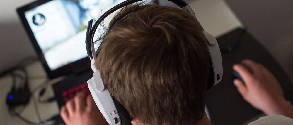 Ein Mann sitzt mit einem Headset vor einem Laptop und spielt ein Online-Computerspiel.