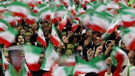 Iranische Flaggen werden während einer Demonstration in die Höhe gehalten.