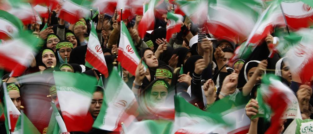 Iranische Flaggen werden während einer Demonstration in die Höhe gehalten.
