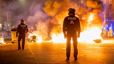 Polizisten stehen vor einer brennenden Barrikade aus Mülltonnen und Mietrollern an der Kreuzung Urbanstraße und Graefestraße.