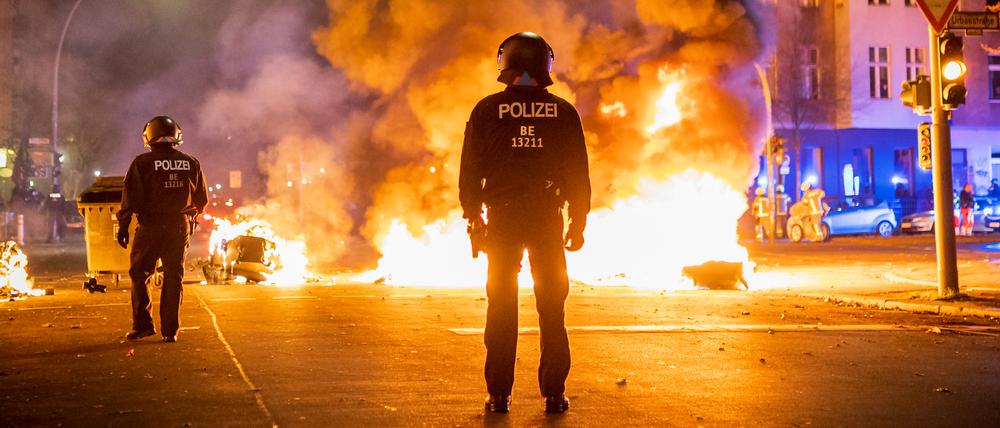 Polizisten stehen vor einer brennenden Barrikade aus Mülltonnen und Mietrollern an der Kreuzung Urbanstraße und Graefestraße.