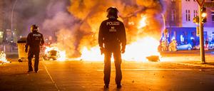 Polizisten stehen vor einer brennenden Barrikade aus Mülltonnen und Mietrollern an der Kreuzung Urbanstraße und Graefestraße.