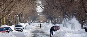 28.12.2022, USA, Buffalo: Ein Anwohner schaufelt Schnee während ein weiterer die verschneite Straße entlang geht. In den USA sind in den vergangenen Tagen bei extremer Kälte und starkem Schneefall mehrere Menschen gestorben. Wintersturm «Elliott» hatte große Teile der USA am Weihnachtswochenende meterhohen Schnee, Temperaturen im zweistelligen Minusbereich und orkanartigen Wind gebracht. Foto: Jeffrey T. Barnes/FR171450 AP/dpa +++ dpa-Bildfunk +++