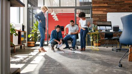 Mixed race group of creative people meeting in the office and discussing. Creative people looking at project plans laying on floor of modern workplace.