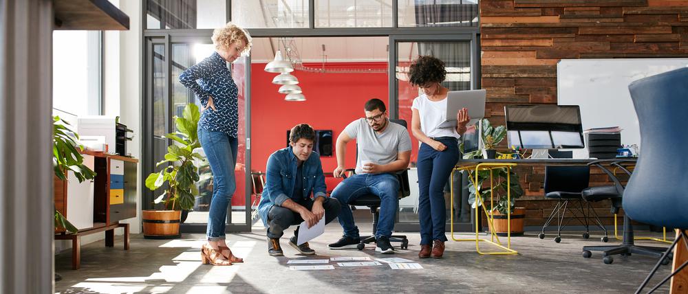 Mixed race group of creative people meeting in the office and discussing. Creative people looking at project plans laying on floor of modern workplace.