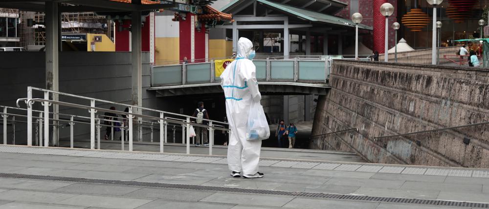 Ein Besucher vom chinesischen Festland steht in voller Schutzkleidung vor dem taoistischen Tempel Wong Tai Shing.