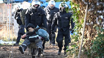 Polizisten schieben einen Klimaaktivisten mit der Schubkarre vom Gelände in Lützerath. Der Energiekonzern RWE will die unter Lützerath liegende Kohle abbaggern.