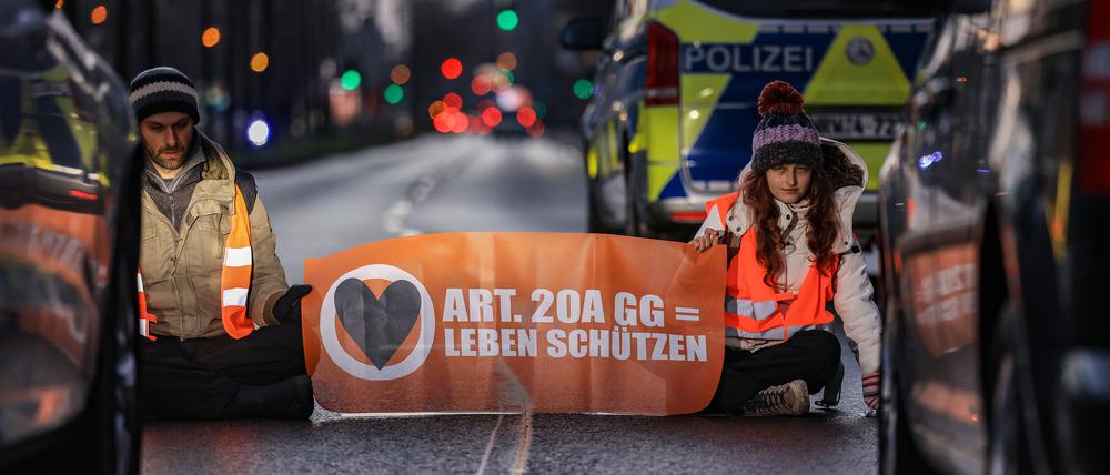 Aktivisten der Umweltschutzorganisation Letzte Generation sitzen vor Fahrzeugen auf einer Straße in Köln.