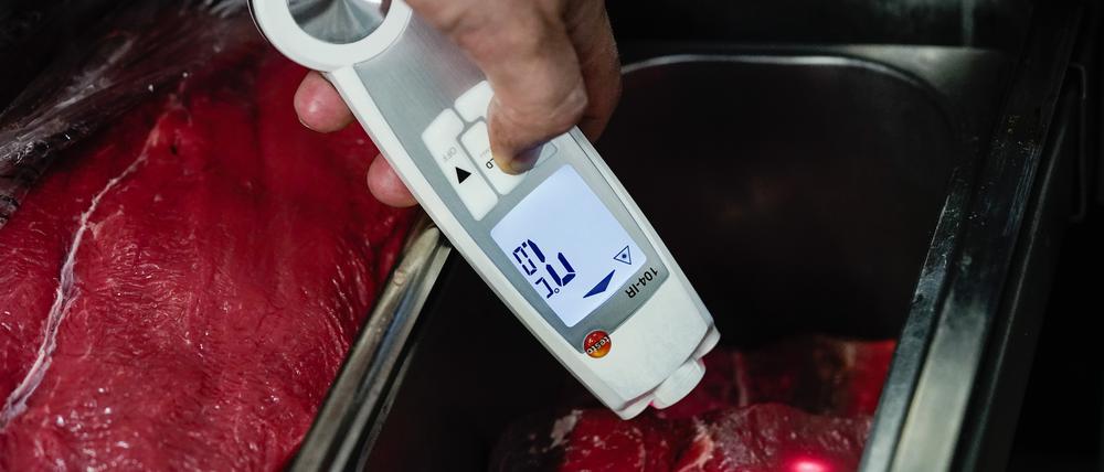 Ein Lebensmittelkontrolleur hält in der Küche eines Restaurants ein Thermometer an Fleischstücke.