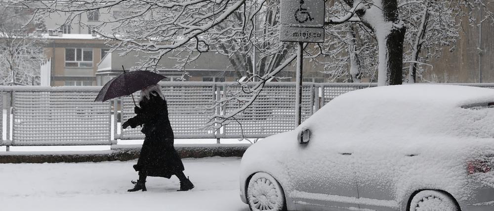 Eine Frau geht in Warschau bei Schneefall auf einem verschneiten Gehweg in Warschau und schützt sich dabei mit einem Regenschirm.