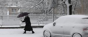 Eine Frau geht in Warschau bei Schneefall auf einem verschneiten Gehweg in Warschau und schützt sich dabei mit einem Regenschirm. 
