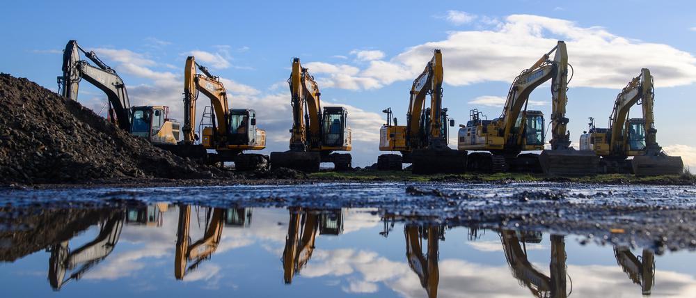 Bagger stehen am Rande eines Ackers nebeneinander und spiegeln sich in einer Pfütze.