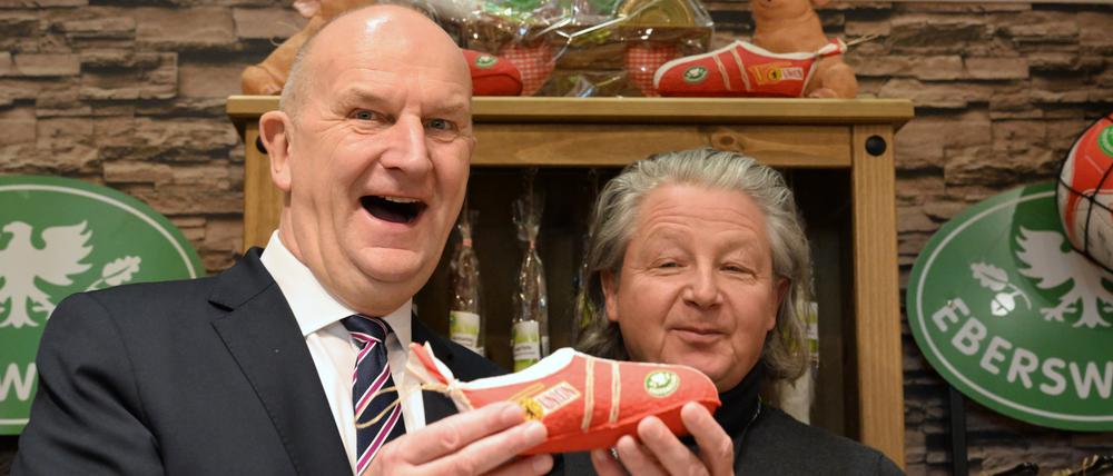 Dietmar Woidke (l, SPD), Ministerpräsident von Brandenburg, hält während der Internationalen Grünen Woche (IGW) zur Eröffnung des Brandenburg-Tages am Stand der Eberswalder Wurst GmbH einen aus Salami geformten Fussballschuh des Bundesligaklubs 1. FC Union Berlin.