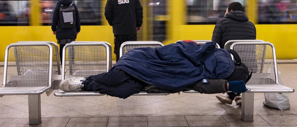 Ein Obdachloser schläft auf einer Bank am Bahnhof Alexanderplatz in Berlin-