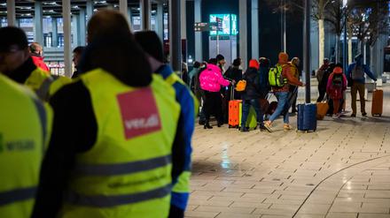 Eine Gruppe mit Rollkoffern geht während eines Warnstreiks am frühen Morgen am Flughafen Berlin-Brandenburg BER an Streikenden vorbei. Die Gewerkschaft Verdi hat am 25. Januar 2023 zu einem ganztägigen Warnstreik am Flughafen Berlin-Brandenburg aufgerufen.