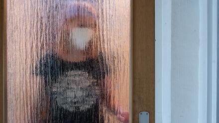 Eine Frau steht während der Isolation nach einem positiven PCR-Test hinter einer Glastür. 