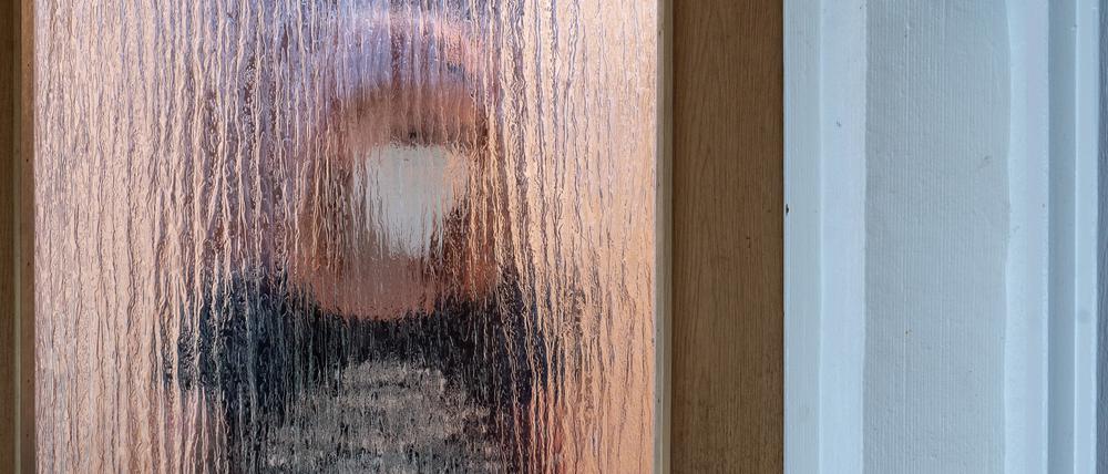 Eine Frau steht während der Isolation nach einem positiven PCR-Test hinter einer Glastür.
