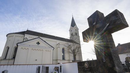 Das Kreuz eines Grabsteins ragt vor der katholische Kirche St. Nikolaus in den Himmel.