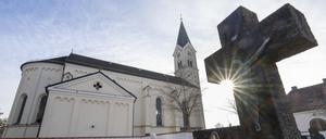 Das Kreuz eines Grabsteins ragt vor der katholische Kirche St. Nikolaus in den Himmel.