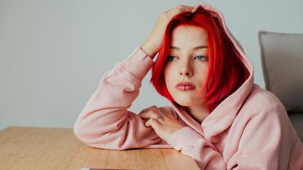 Portrait of a sad teen bored girl holding head on desk waiting for text message on cell phone device looking at window