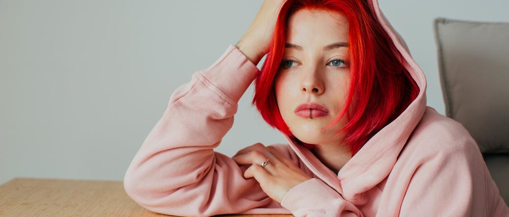 Portrait of a sad teen bored girl holding head on desk waiting for text message on cell phone device looking at window