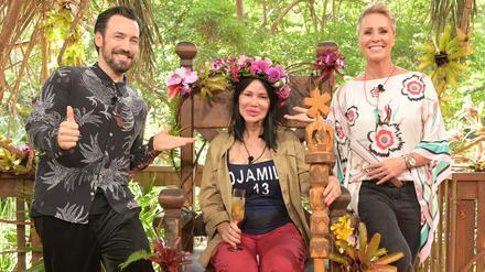 Visagistin Djamila Rowe sitzt mit ihrer Krone nach dem Sieg beim RTL-Dschungelcamp 2023 auf ihrem Thron neben der Moderatorin Sonja Zietlow (r) und Moderator Jan Köppen.  