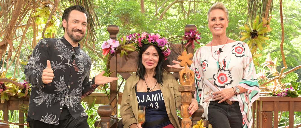 Visagistin Djamila Rowe sitzt mit ihrer Krone nach dem Sieg beim RTL-Dschungelcamp 2023 auf ihrem Thron neben der Moderatorin Sonja Zietlow (r) und Moderator Jan Köppen.  