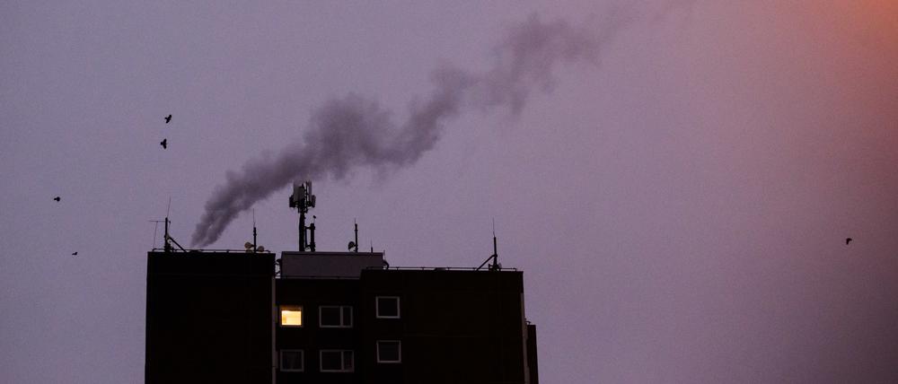 Nur in einer Wohnung eines Mehrfamilienhauses brennt am frühen Morgen Licht, während von einer Heizungsanlage Dampf aufsteigt.