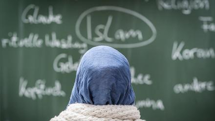 Eine junge Frau mit Kopftuch sitzt in einer Schule vor einer Tafel. Das Land Berlin darf Lehrerinnen nicht pauschal das Tragen von Kopftüchern verbieten. 