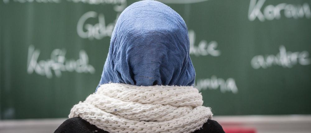 Eine junge Frau mit Kopftuch sitzt in einer Schule vor einer Tafel. Das Land Berlin darf Lehrerinnen nicht pauschal das Tragen von Kopftüchern verbieten.