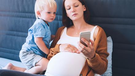 Eine schwangere Frau und ein Kleinkind blicken auf ein Smartphone: Banken und Neobroker bieten Kinderdepots an, die Eltern verwalten können. 