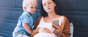 Eine schwangere Frau und ein Kleinkind blicken auf ein Smartphone: Banken und Neobroker bieten Kinderdepots an, die Eltern verwalten können. 