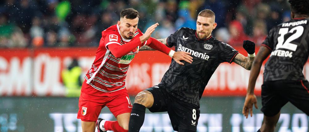 Mergim Berisha vom FC Augsburg (l) und Robert Andrich von Bayer Leverkusen im Zweikampf um den Ball.