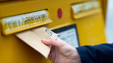 Ein Mann wirft einen Brief in einen Briefkasten (Symbolbild).