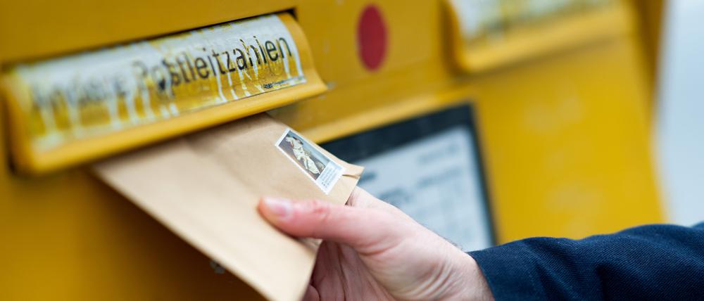 Ein Mann wirft einen Brief in einen Briefkasten.
