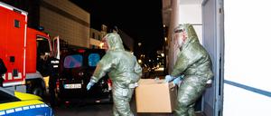 Männer in Schutzanzügen tragen einen Karton aus dem Haus, in dem ein Anti-Terror-Einsatz stattfand.