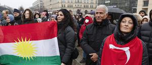 Trauernde haben sich zu einer Gedenkveranstaltung für die Opfer des Erdbebens in der Türkei und Syrien am Brandenburger Tor versammelt und ziegen eine kurdische und eine türkische Flagge. 