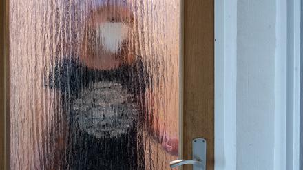 Eine Frau steht während der Isolation nach einem positiven PCR-Test hinter einer Glastür. 