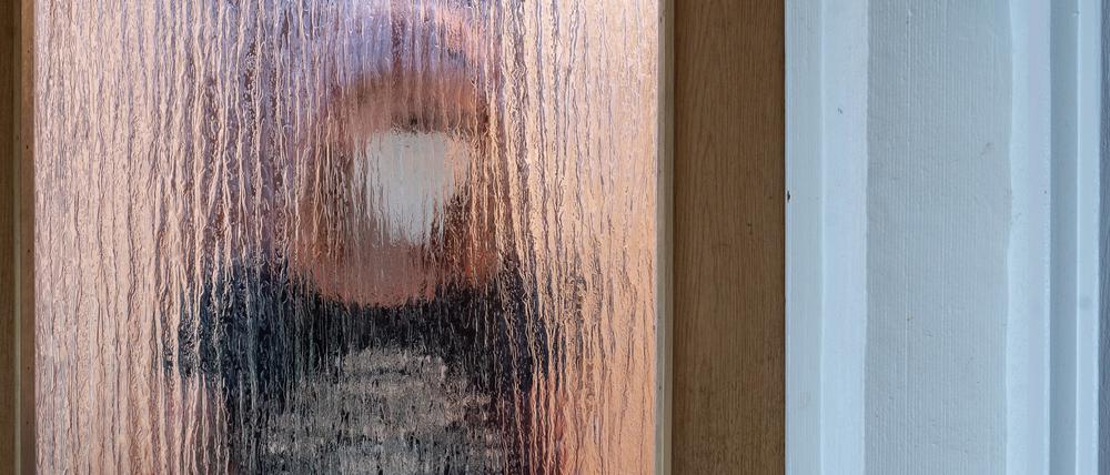 Eine Frau steht während der Isolation nach einem positiven PCR-Test hinter einer Glastür. 