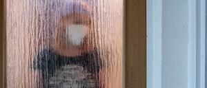 Eine Frau steht während der Isolation nach einem positiven PCR-Test hinter einer Glastür. 