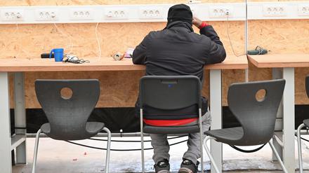 Ein Geflüchteter ist in einem Zelt der Flüchtlingsunterkunft mit seinem Smartphone beschäftigt. 
