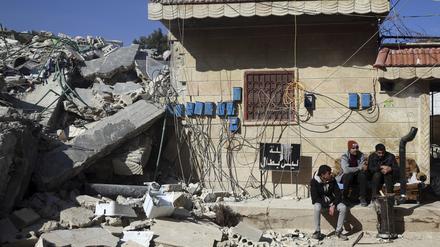 Menschen sitzen vor einem eingestürztem Gebäude im syrischen Jinderis.
