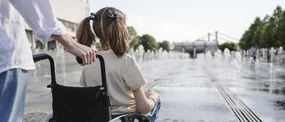 Mother standing behind daughter with disability sitting in wheelchair at park on sunny day model released, Symbolfoto, EYAF01974
