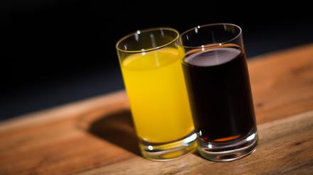 ARCHIV - 29.03.2016, Hamburg: ILLUSTRATION - Ein Glas mit Cola steht neben einem Glas mit Orangenlimonade. Verbraucherschützer und Gesundheitsexperten fordern verbindlichere Vorgaben und mehr Tempo, um zu weniger Zucker in Erfrischungsgetränken wie Cola oder Limonaden zu kommen. (zu dpa «Rufe nach mehr Tempo bei Zuckerreduktion in Limonaden») Foto: Lukas Schulze/dpa +++ dpa-Bildfunk +++