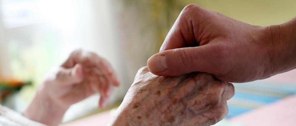 Ein Pfleger hält in einem Pflegeheim die Hand einer Bewohnerin. 