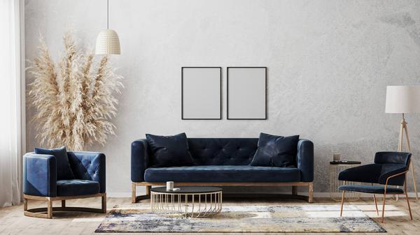 Ein modern eingerichtetes Wohnzimmer mit einem blauen Sofa und zwei blauen Sesseln vor einer grauen Wand (Symbolbild)