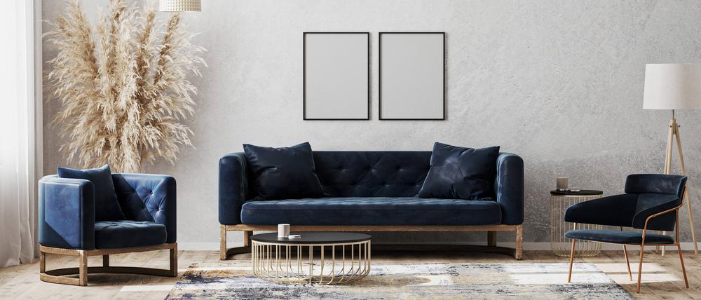 Ein modern eingerichtetes Wohnzimmer mit einem blauen Sofa und zwei blauen Sesseln vor einer grauen Wand (Symbolbild)