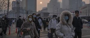 Pendler tragen Gesichtsmasken und überqueren eine Kreuzung während des morgendlichen Berufsverkehrs. 