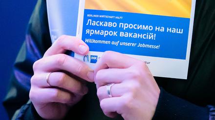 Eine Frau hält bei einer Jobmesse für ukrainische Geflüchtete von der IHK Berlin und der Agentur für Arbeit den Messeplan mit der ukrainischen Flagge.